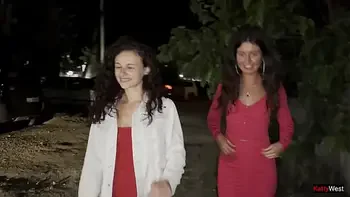 Two girlfriends pee together near a car in a public parking lot