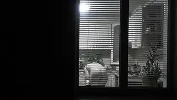 Peeping. Voyeur. Neighbor pervert voyeur in evening on street looks out window as naked sexy neighbor in kitchen prepares dinner for her husband. Naked in public. Naked at home. Family.  Outdoor